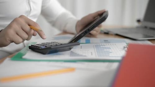 Close Up of Person Using Calculator and Tablet