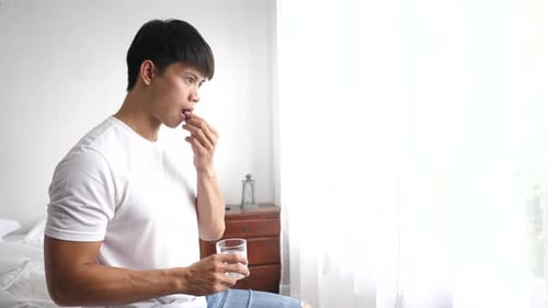 Young Man Takes Pill with Water Indoors