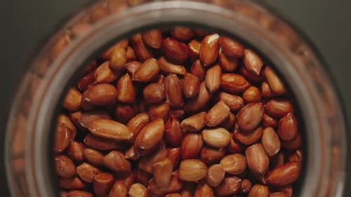 TOP VIEW: Peeled Peanuts Falling Into A Glass Jar - Slow Motion
