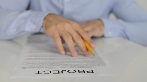 Person Reviews Project Document at Desk with Pencil