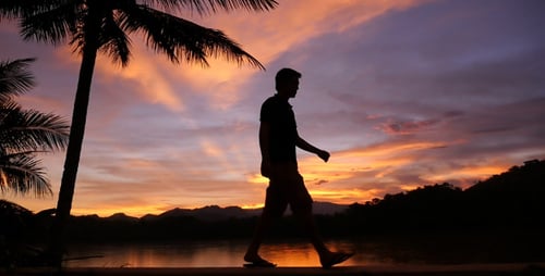 Silhouetted Man Walks Along Tropical Beach at Sunset