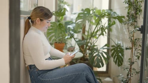 Woman Uses Phone Surrounded by Plants Indoors