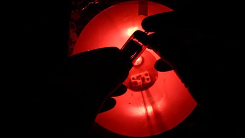 Hands Manipulating Vacuum Tube Against a Red Light