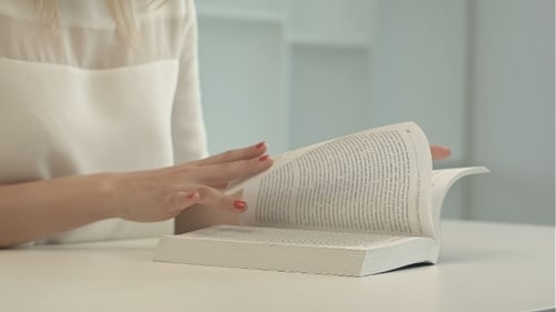 Woman Reads Book and Turns Pages at Table