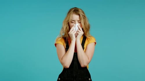 Une femme malade éternue dans les tissus. Isolé sur fond bleu de studio. La fille est malade, a un rhume ou