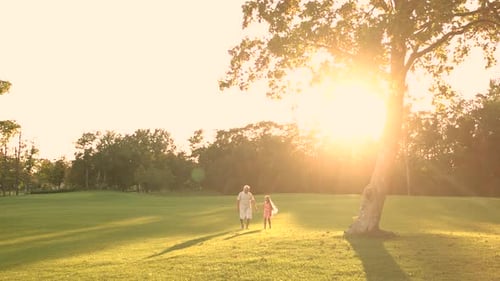 Grandfather and Granddaughter Walking in Sunset Field