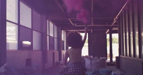 Mixed race woman holding purple flare running through an empty building