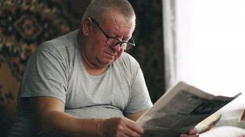 Senior Man Reading Newspaper Indoors By Window