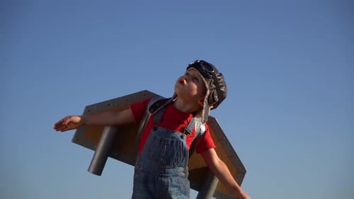 Glückliches Kind mit Spielzeug-Papier-Jetpack spielt gegen blauen Himmel