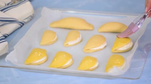 Pastry chef smearing egg yolk on raw bun with silicone brush.