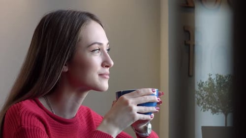 Young Woman Drinking Coffee in Cafe by Window