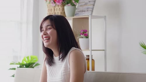 Asian woman happy laughing on indoor sofa at home in casual dress on morning