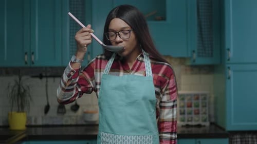 Woman Tasting Food from Spoon in Kitchen