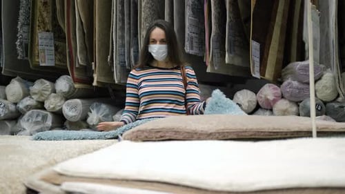 Woman in Protective Mask Choosing Carpet in Store