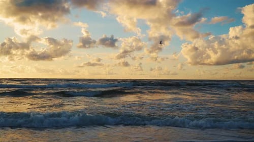 Sunset behind Clouds over Sea Waves and Sandy Beach