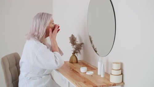 Woman Applying Lotion to Face in Mirror