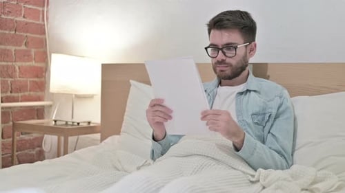 Man Reading Documents in Bed at Home