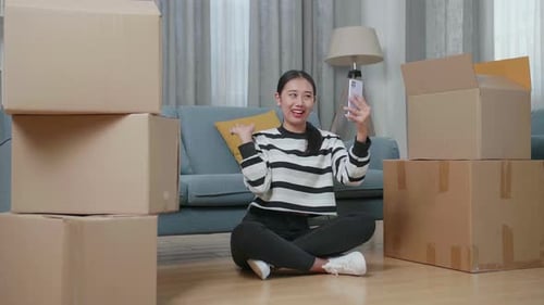 Asian Woman With Cardboard Boxes Live Stream By Smartphone After Moving Into A New House