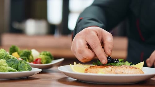 Close Up Male Chef Hand Putting Black Olive on Salmon Steak Serving Plate