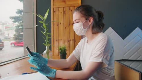 Woman Wearing Mask Using Phone at Table Indoors