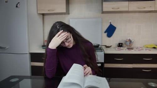 Girl Sits in the Kitchen in the Evening Leafing Through a Textbook and Cannot Figure It Out