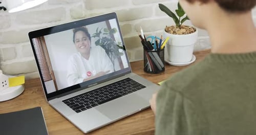 Jeune homme agitant la main et parlant lors d'un appel vidéo avec une collègue de sexe féminin via un ordinateur portable