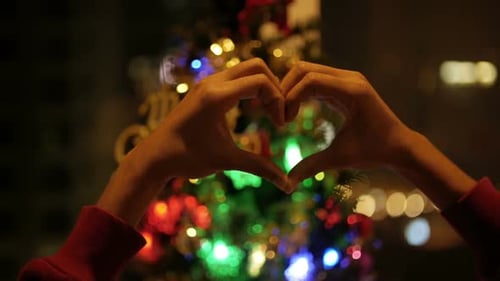 Hands make heart shape in front of Christmas Tree