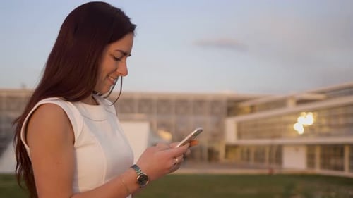 Side View of Smiling Young Texting on Smartphone Outdoor
