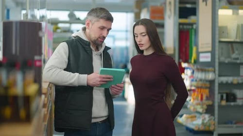 Confident Caucasian Man Consulting Young Charming Woman Choosing Supplies in Hardware Store