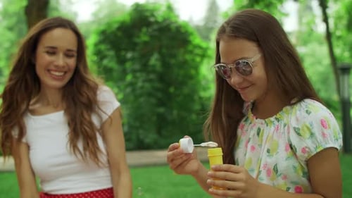 Woman and Girl Playing with Soap Bubbles in Park. Family Laughing Outdoors