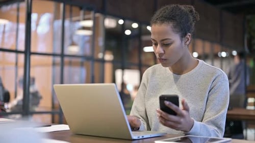 Woman Using Smartphone and Laptop in Modern Office