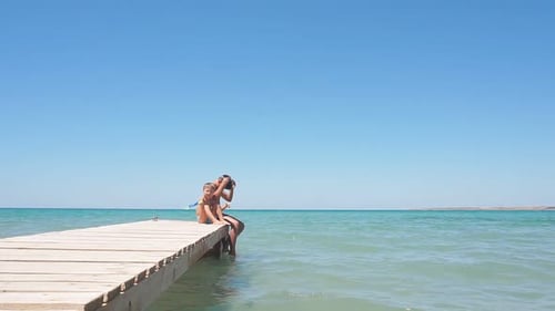 Tanned Boys and Children Dressed in Swimming Shorts Sit on a Wooden Pier on a Sunny Summer Day