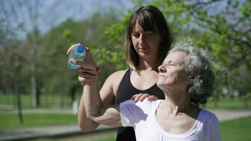 Woman Helping Senior with Light Exercises in Park
