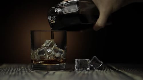 Pouring Whiskey, Cognac Into Glass. Dark Background. Pour of Alcohol Drink