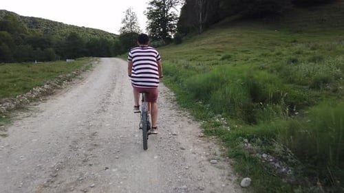 Nahaufnahme eines männlichen Radfahrers, der von hinten auf einer Landstraße gefilmt wurde. Mann in lässiger Sommerkleidung los