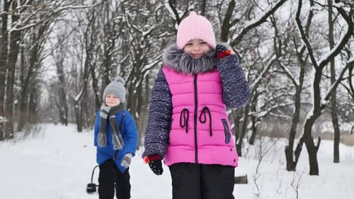 Kinder, ein Junge und ein Mädchen im Wald im Winter, springen, werfen Schnee und lachen