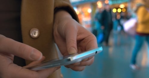 Frau tippt auf Handy am Bahnhof