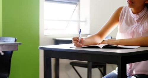Girl Writing in a Notebook at School Desk