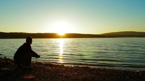 Man Skipping Stones at Sunset on a Calm Lake