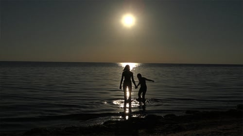Woman and Child Standing in Sunlit Ocean