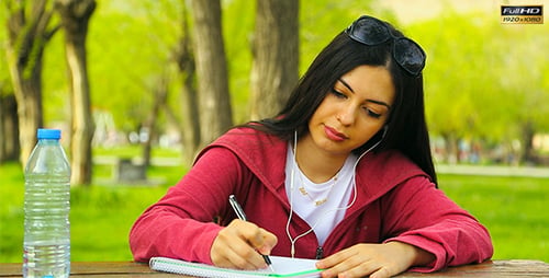 Young Woman Writing in Park with Earbuds