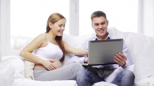 Expecting Couple Relaxing with Laptop on Sofa