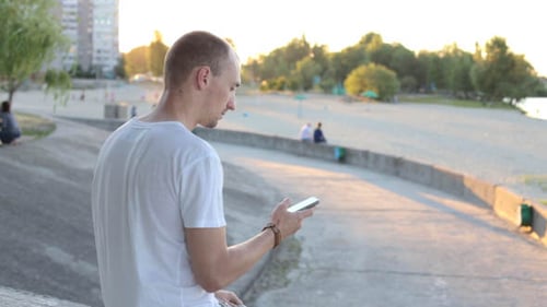 Young Adult Using Cellphone at the Beach at Sunset