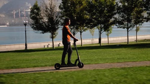 Ein Mann fährt am sonnigen Morgen Elektroroller im Stadtpark