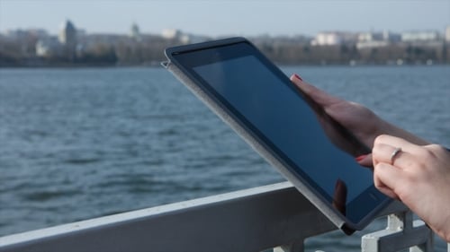 Woman Using Tablet Outdoors Near City and Water