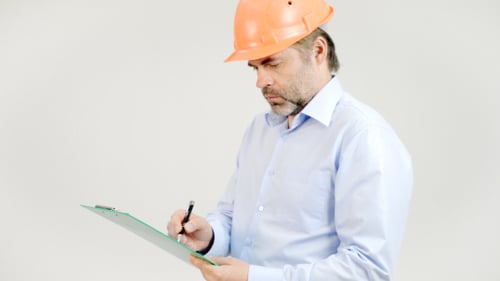 Engineer Writing on Clipboard With Orange Helmet