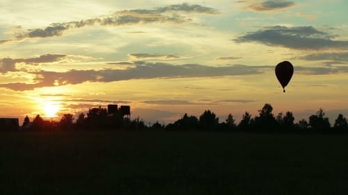 Hot Air Balloon Flying Over Field at Sunset
