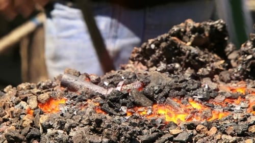 Blacksmith Heating Metal in Glowing Coal Forge