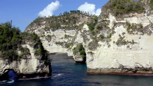Diamond Beach in Nusa Penida island with natural rock arch and tall rock formations, Aerial dolly ou