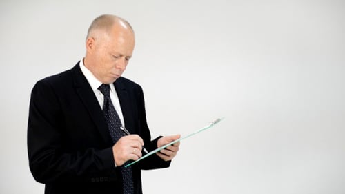 Man in Suit Writing on Clipboard